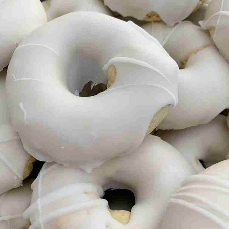 Donuts covered in smooth white icing are piled closely together, highlighting their glossy texture and soft appearance.