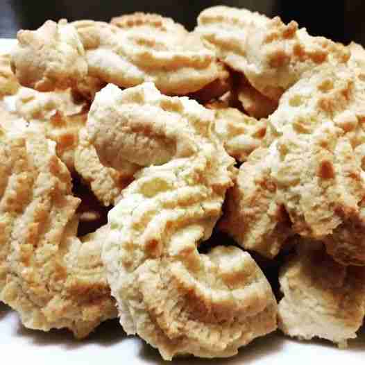 A pile of light brown, intricately ridged cookies sits on a plate. They appear freshly baked, with a slightly crumbly texture, in a kitchen setting.